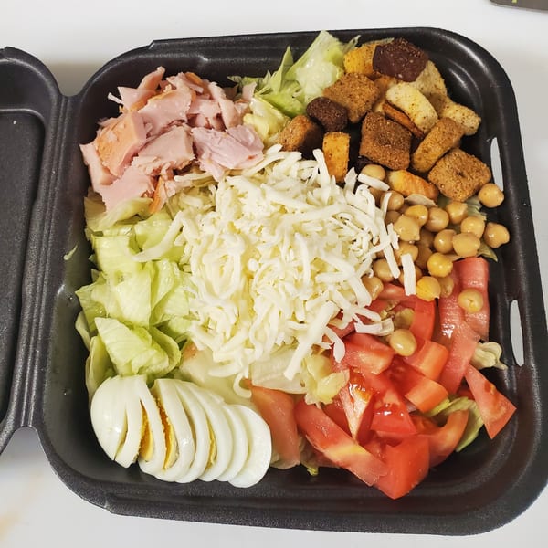 A Dough Boys Pizzeria salad with ham, cheese, chickpeas, croutons, tomatoes, lettuce, and sliced egg.