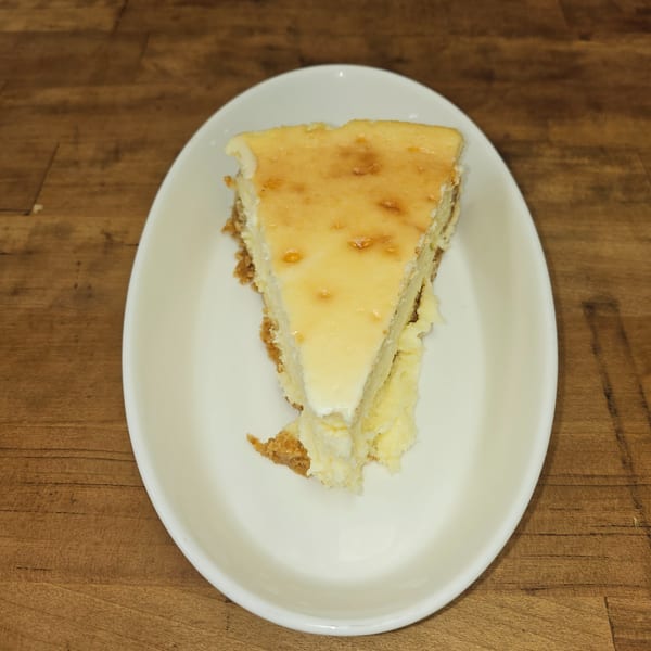 A slice of classic cheesecake with a golden-brown top and graham cracker crust on a white plate.
