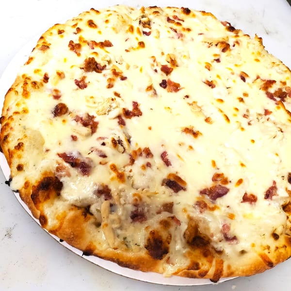 A Dough Boys Pizzeria white pizza with melted cheese and bacon bits on a white surface.