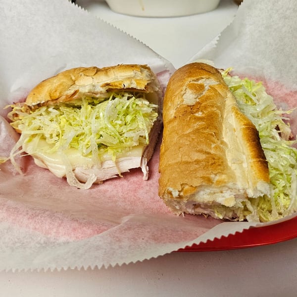 Two halves of a Dough Boys Pizzeria sub sandwich with meat, cheese, and shredded lettuce.